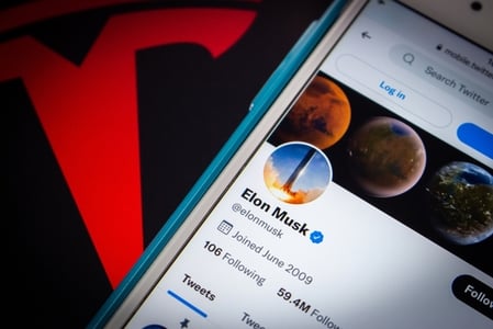 Elon Musks Twitter profile displays on a mobile phone sitting next to the Tesla logo